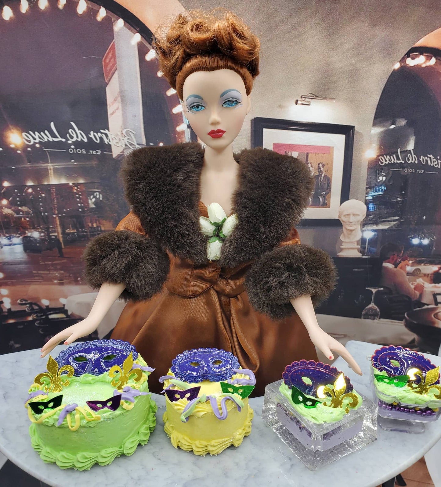 Chef Gina's Mardi Gras doll cake featuring a stylish doll with brown fur coat and colorful Mardi Gras themed mini cakes