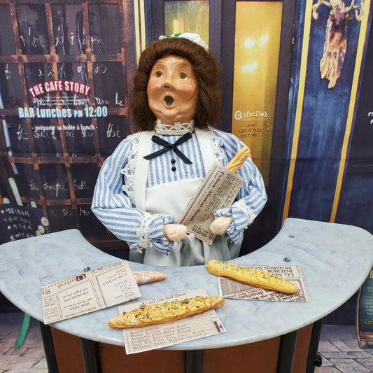 Chef Gina's miniature baguette bread model scene with doll holding bread wrapped in newspaper