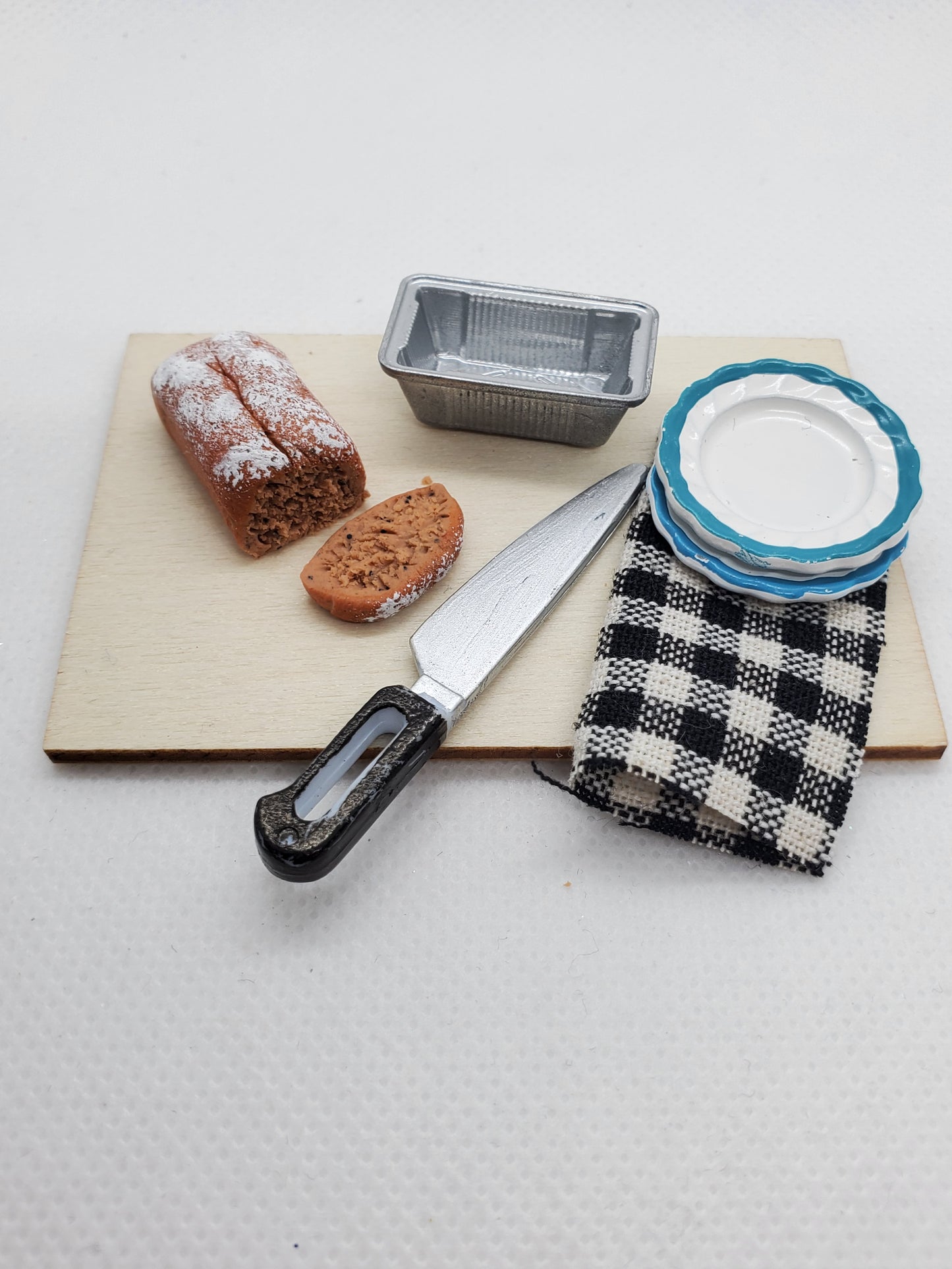 Miniature banana bread for dolls with slice, knife, and plates on a wooden cutting board