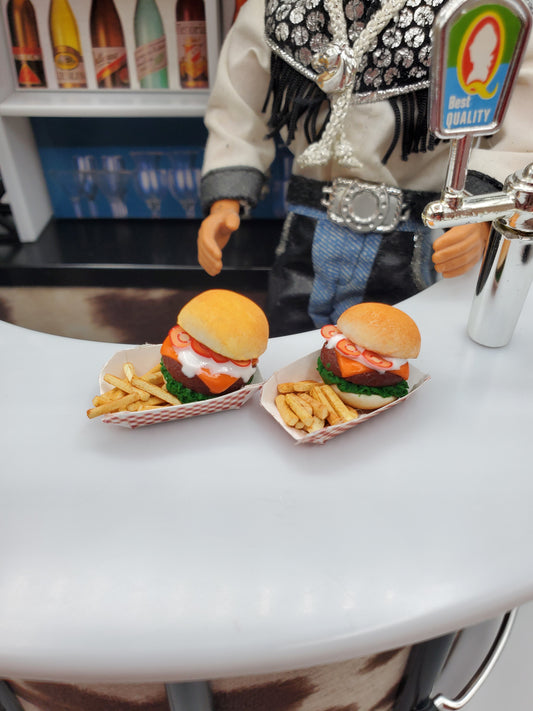 Two miniature bison burgers for dolls served with fries on a white counter next to a doll figure