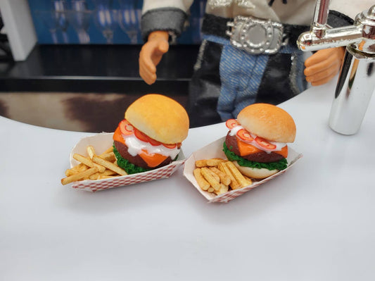 Two miniature bison burgers for dolls served with fries on a white counter next to a doll figure