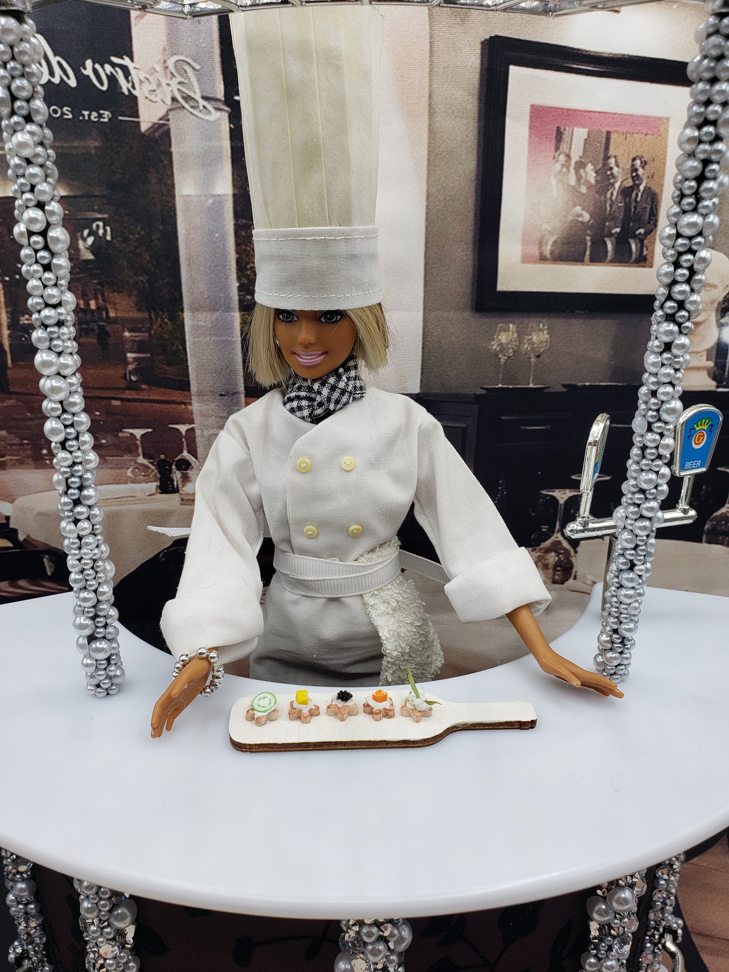 Chef doll presenting a miniature hors d'oeuvres platter with assorted small appetizers on a white table