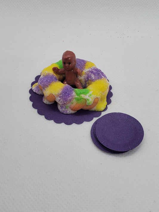 Miniature Mardi Gras king cake topped with a baby figurine and colorful sprinkles on a purple base