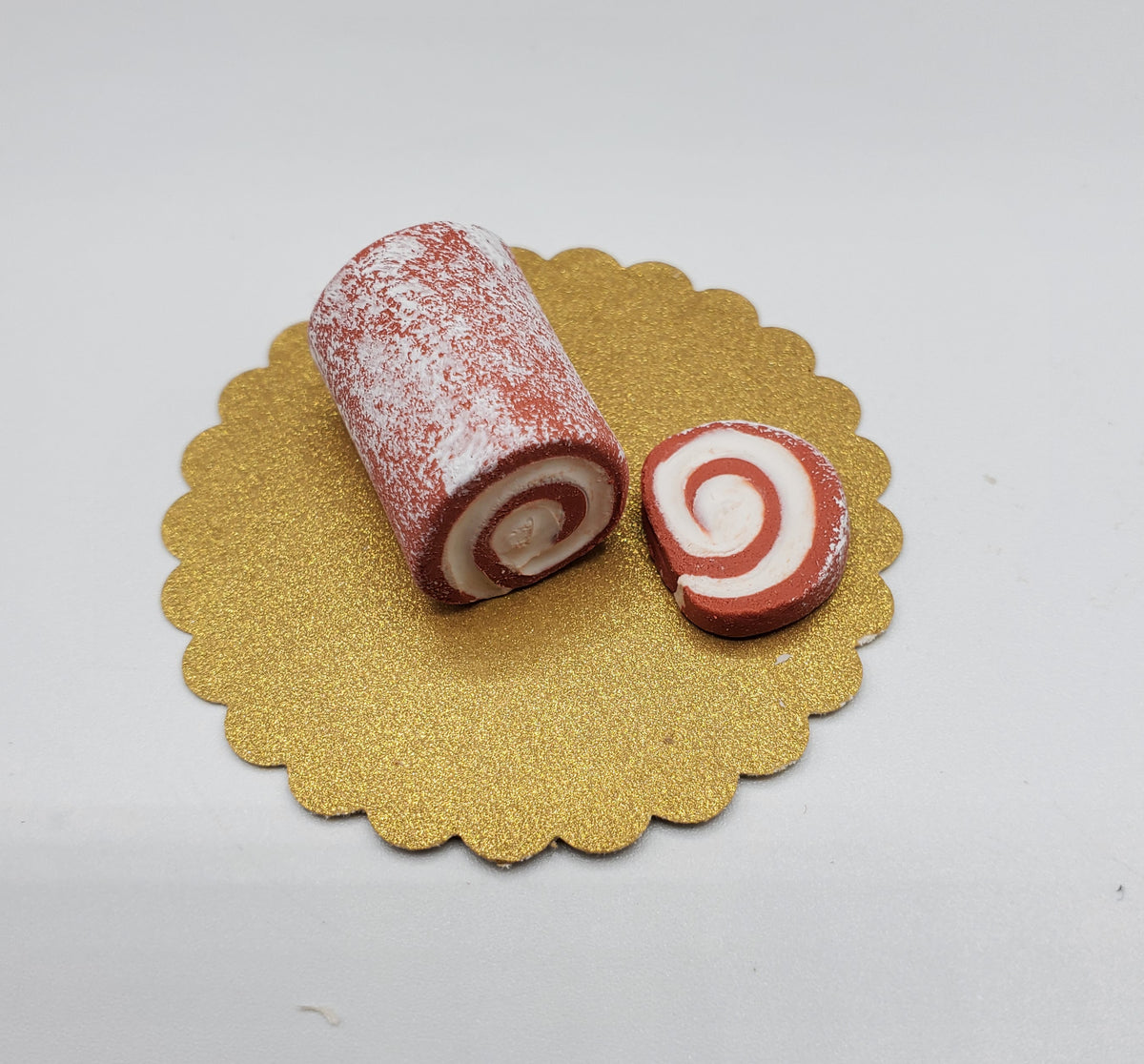 Miniature pumpkin roll for dolls on a gold scalloped plate with a slice cut out