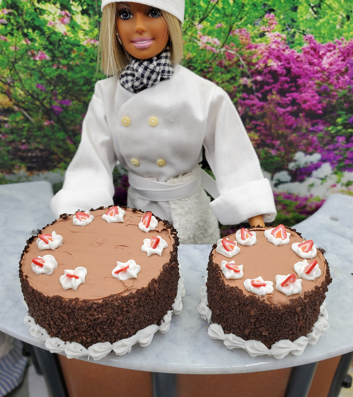 Two miniature spring chocolate cakes decorated with white frosting and vibrant flowers in the background