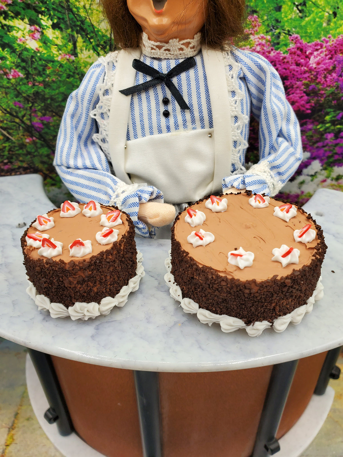 Miniature spring chocolate cake decorated with icing and strawberries, showcased by a chef doll