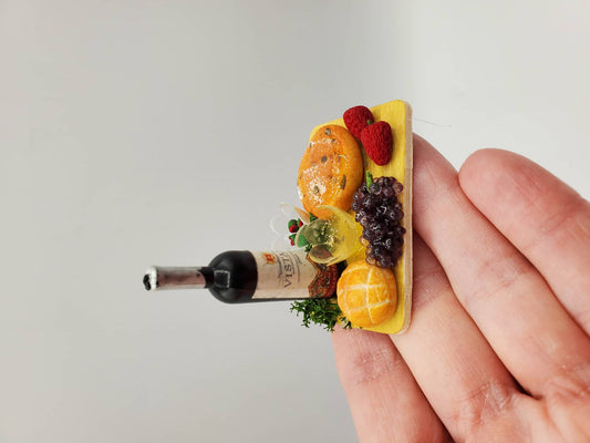 Miniature wine cheese tray with bottle of wine, grapes, bread, and raspberries held on fingertip