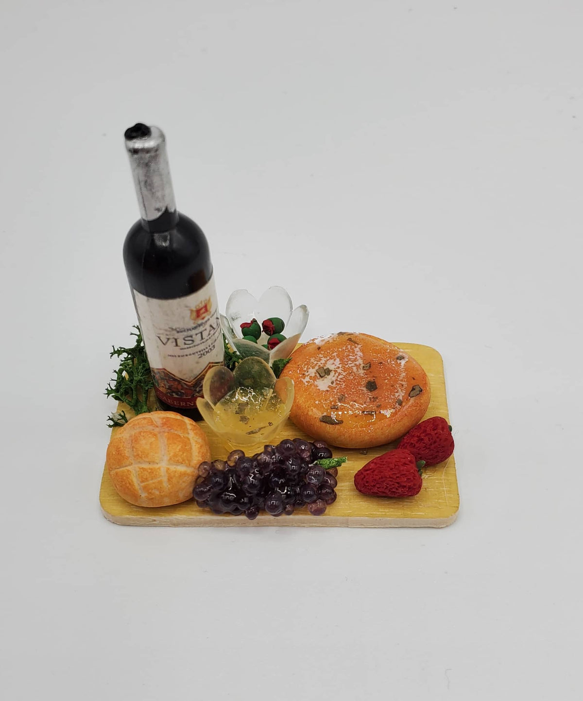 Chef Gina's miniature wine cheese tray with a bottle of red wine, cheese rounds, grapes, and berries on a wooden board