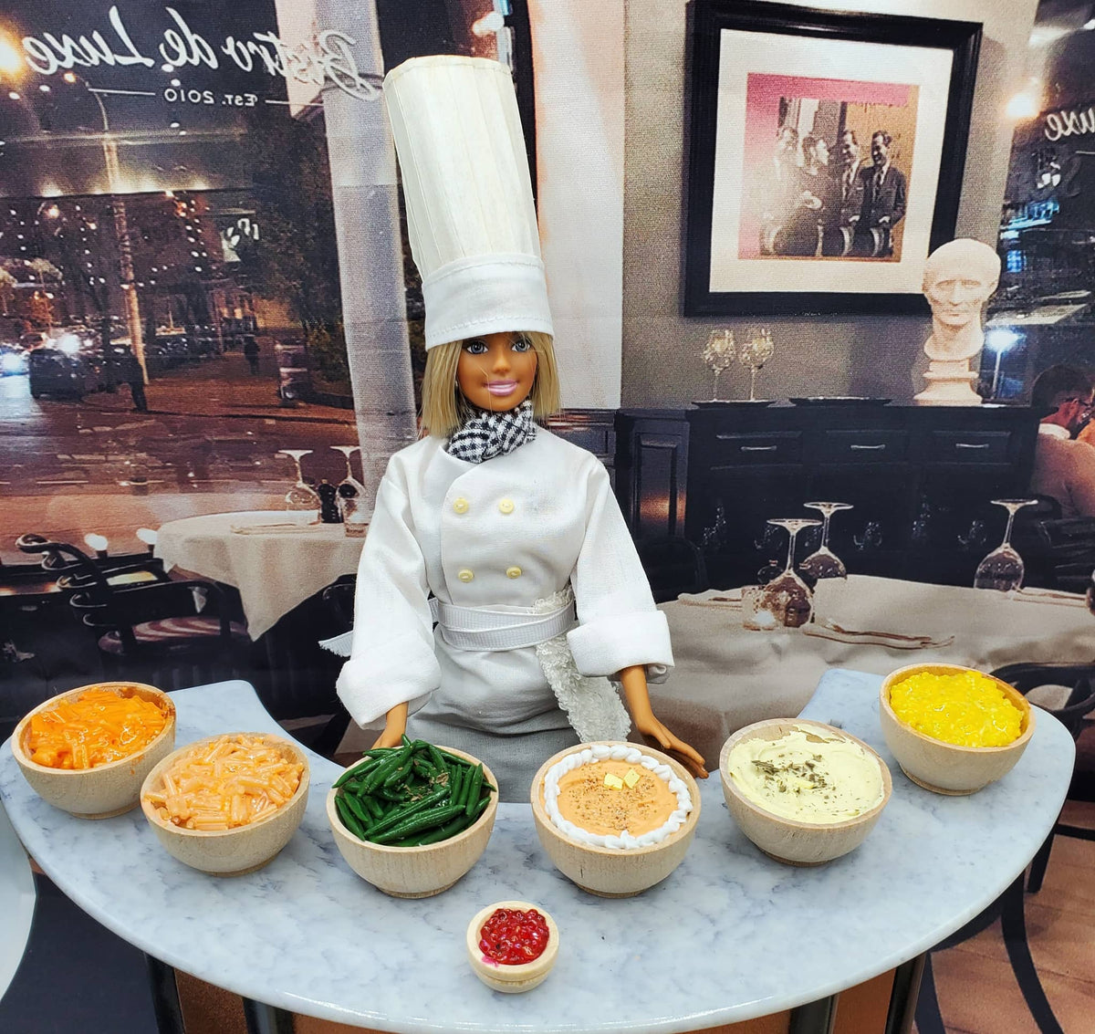 Chef doll standing behind bowls of miniature Yukon Gold mashed potatoes and other side dishes on a marble table