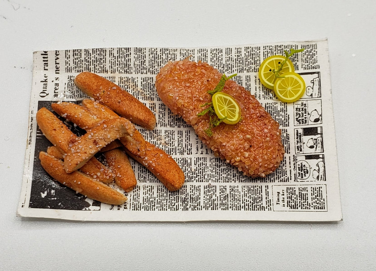 Miniature fried fish for dolls served with fries and lemon slices on a newspaper plate