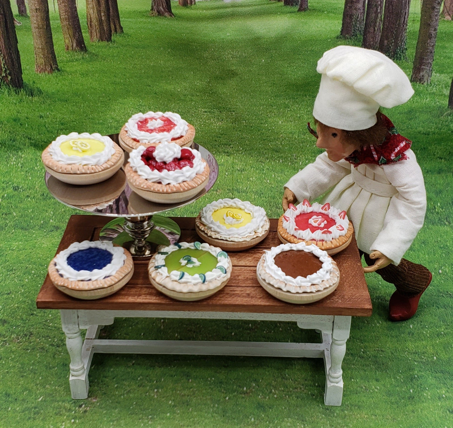 One sixth scale chocolate pie displayed among colorful dessert pies on a wooden table in a scenic forest setting