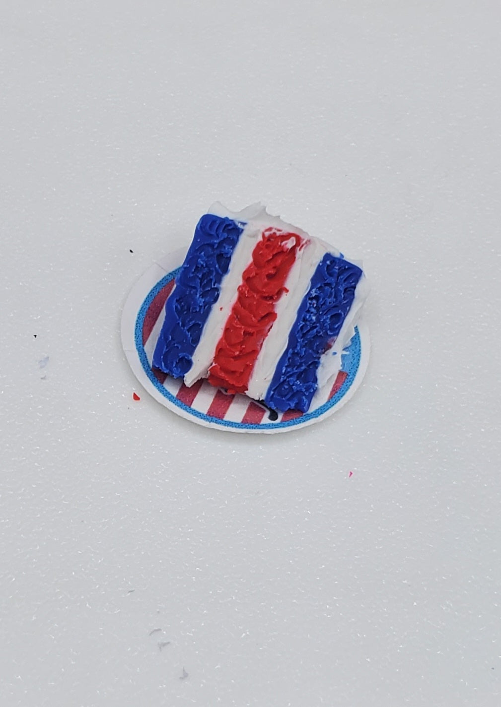 Small cake with red, white, and blue frosting on a white plate against a light gray background
