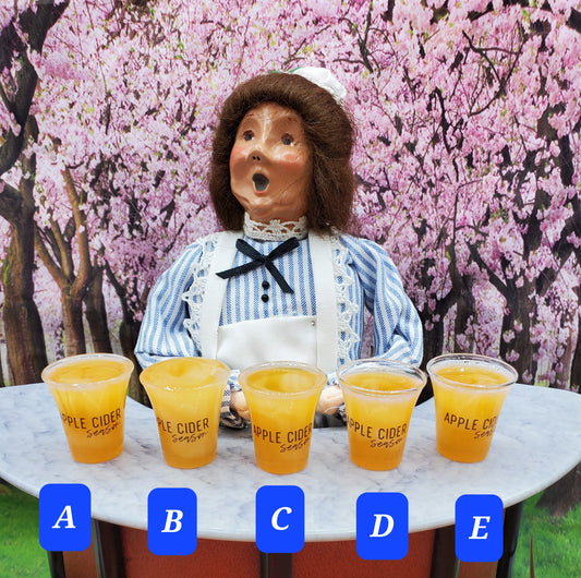 Chef Ginas Mini Food doll apple cider drinks in small cups labeled A to E on marble table with cherry blossom background