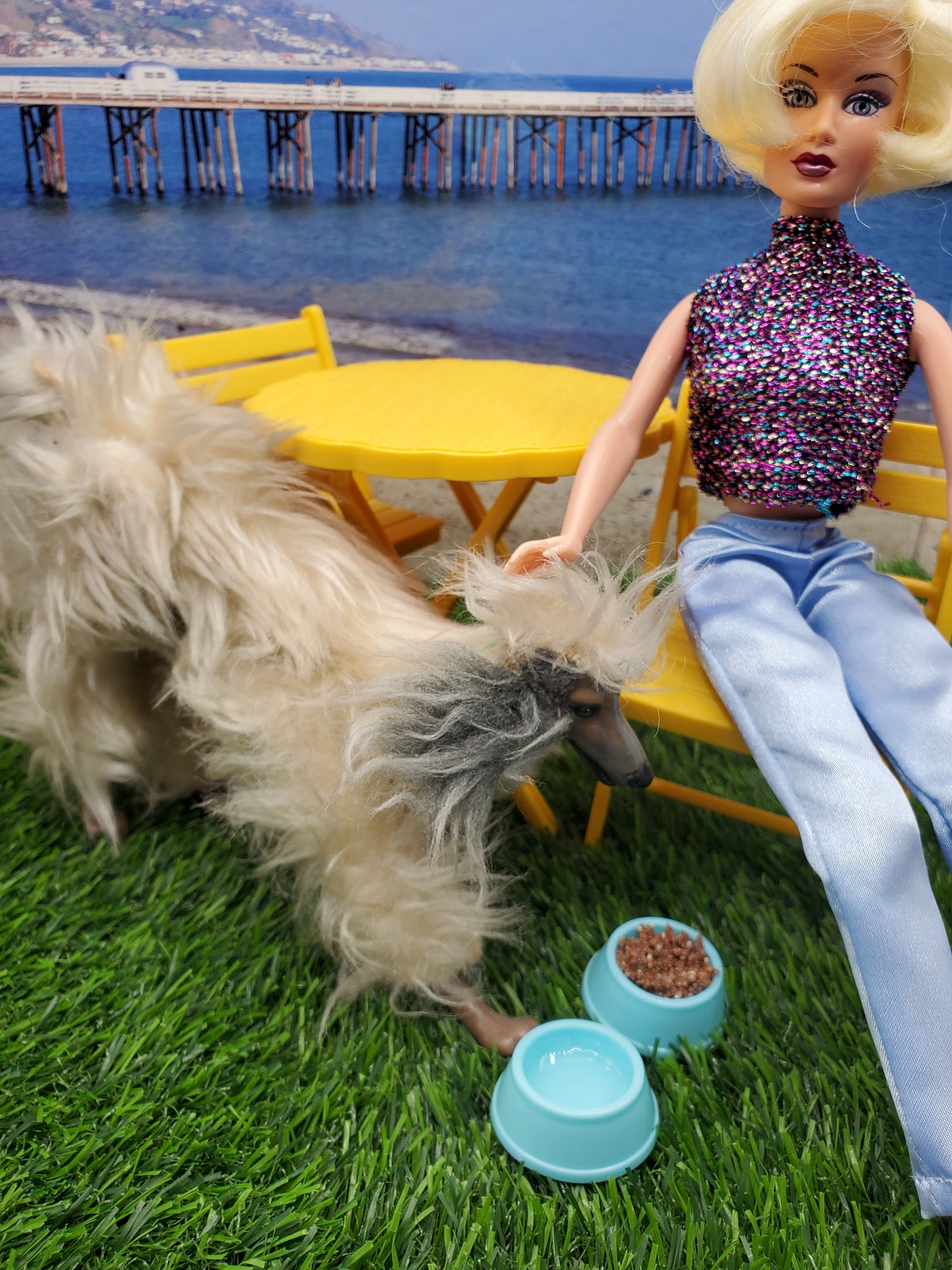 Fashion doll dog food bowls placed next to a stylish doll and a furry dog on a sunny patio