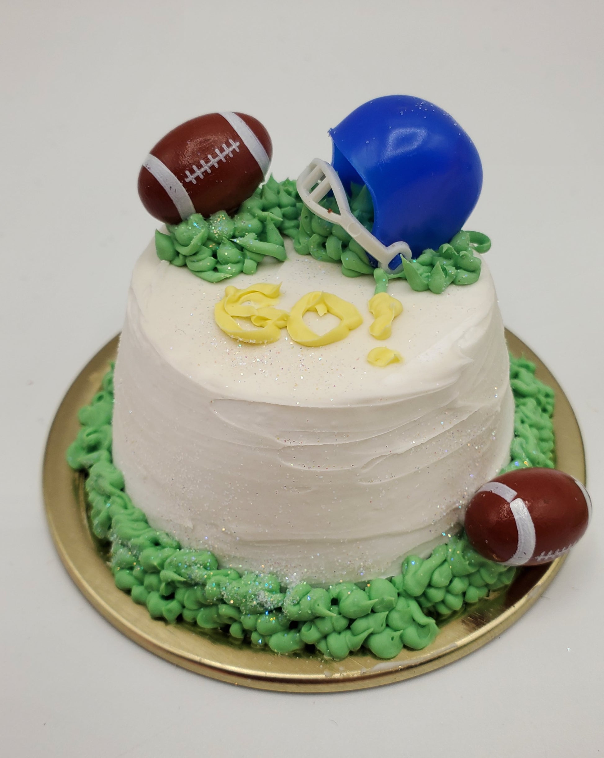 Chef Gina's mini cake decorated with football party doll accessories including a blue helmet and two footballs on white frosting