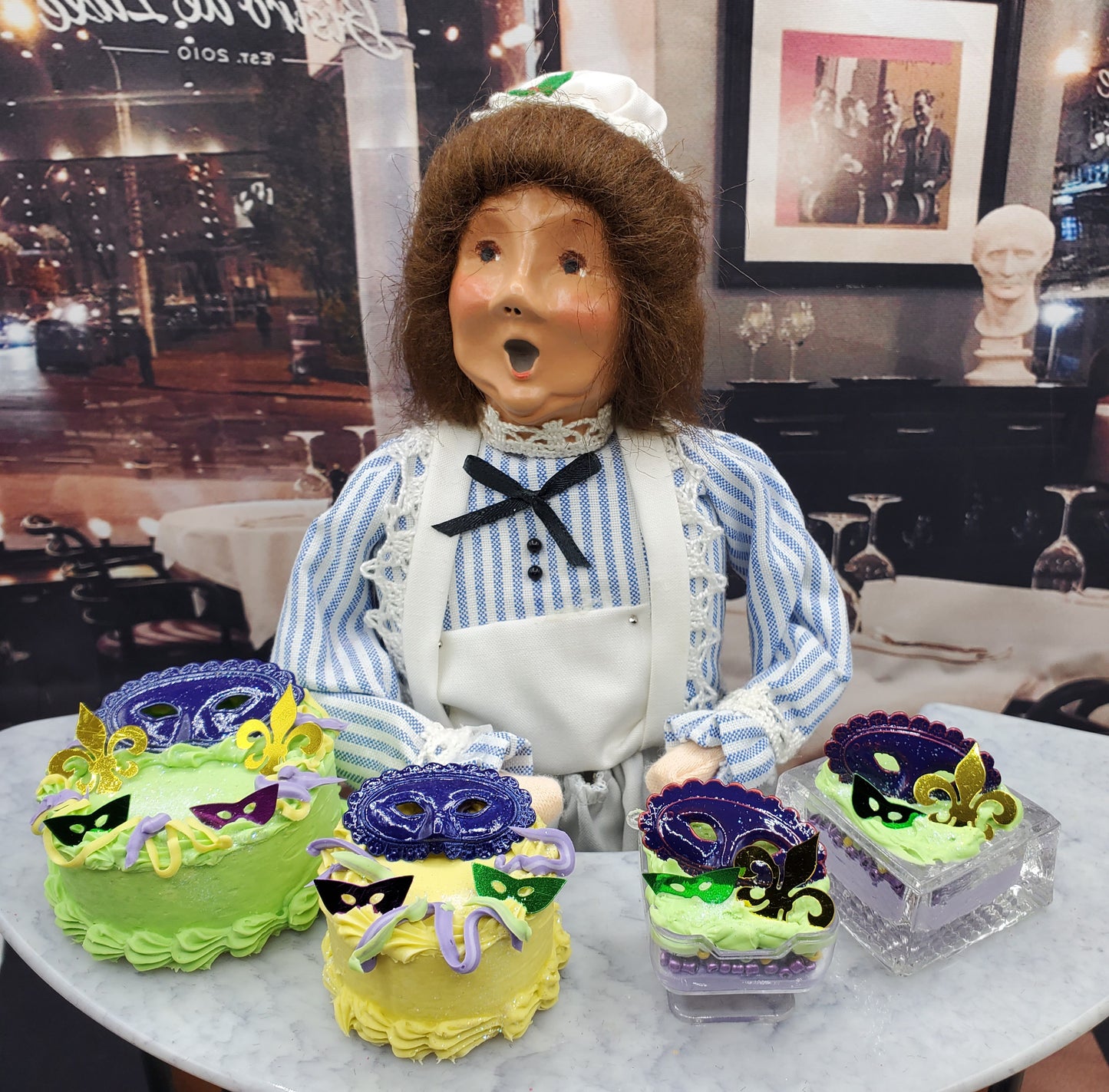 Chef Gina's Mardi Gras doll cake display with green and yellow mini cakes decorated with purple masks and fleur de lis