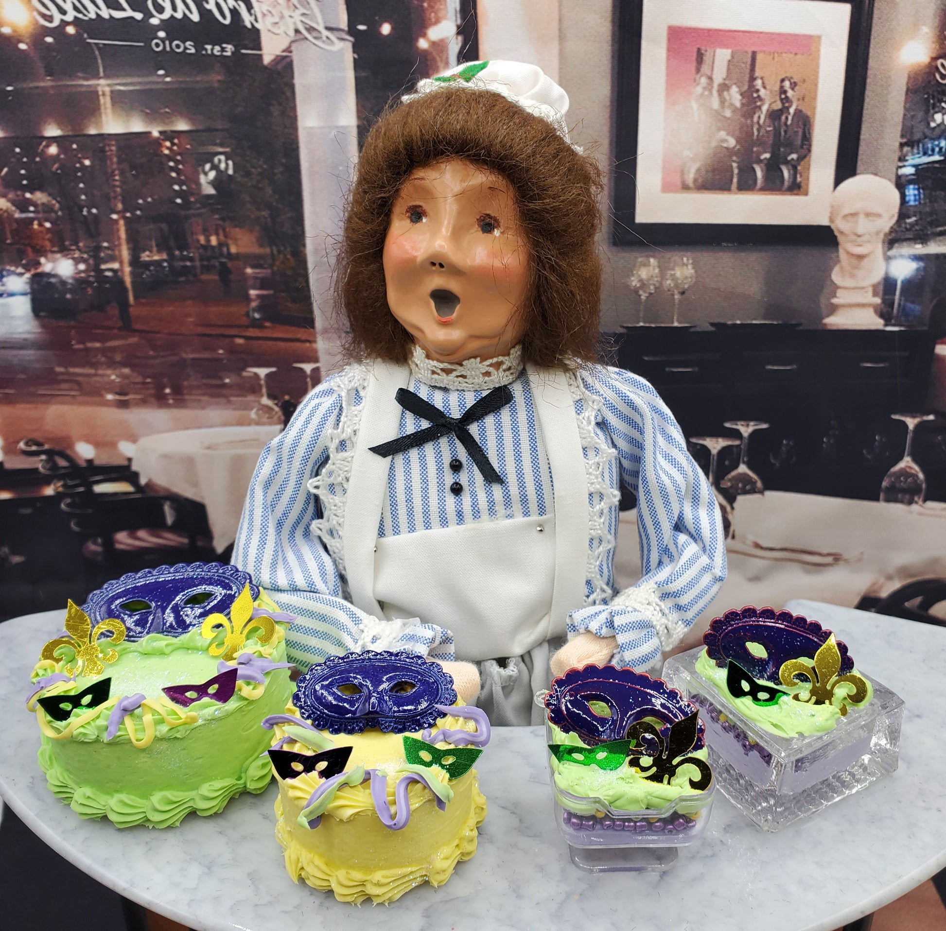 Chef Gina's Mardi Gras doll cake display with green and yellow mini cakes decorated with purple masks and fleur de lis