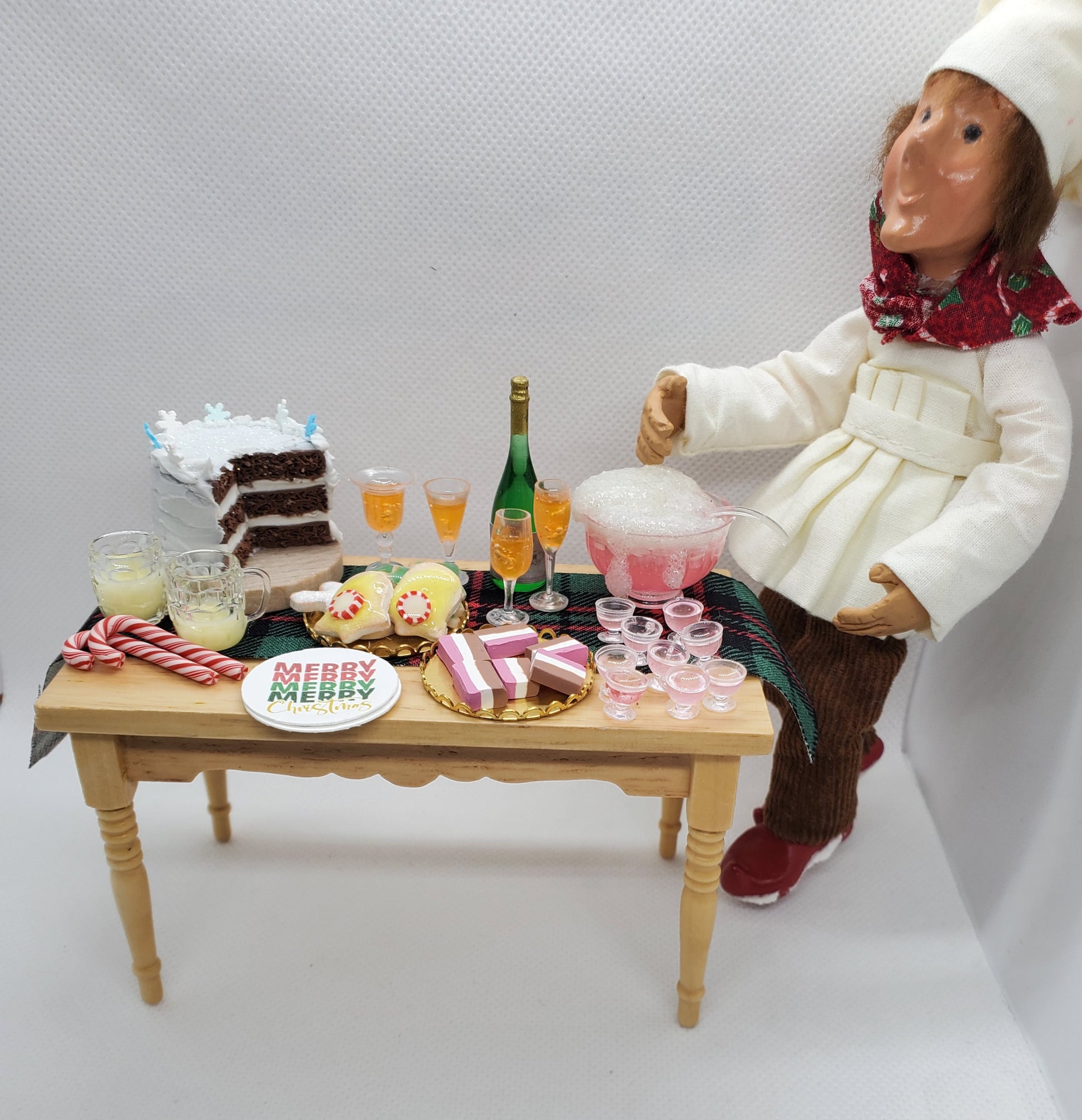 1:12 scale doll furniture wooden table with miniature holiday treats and drinks next to chef doll