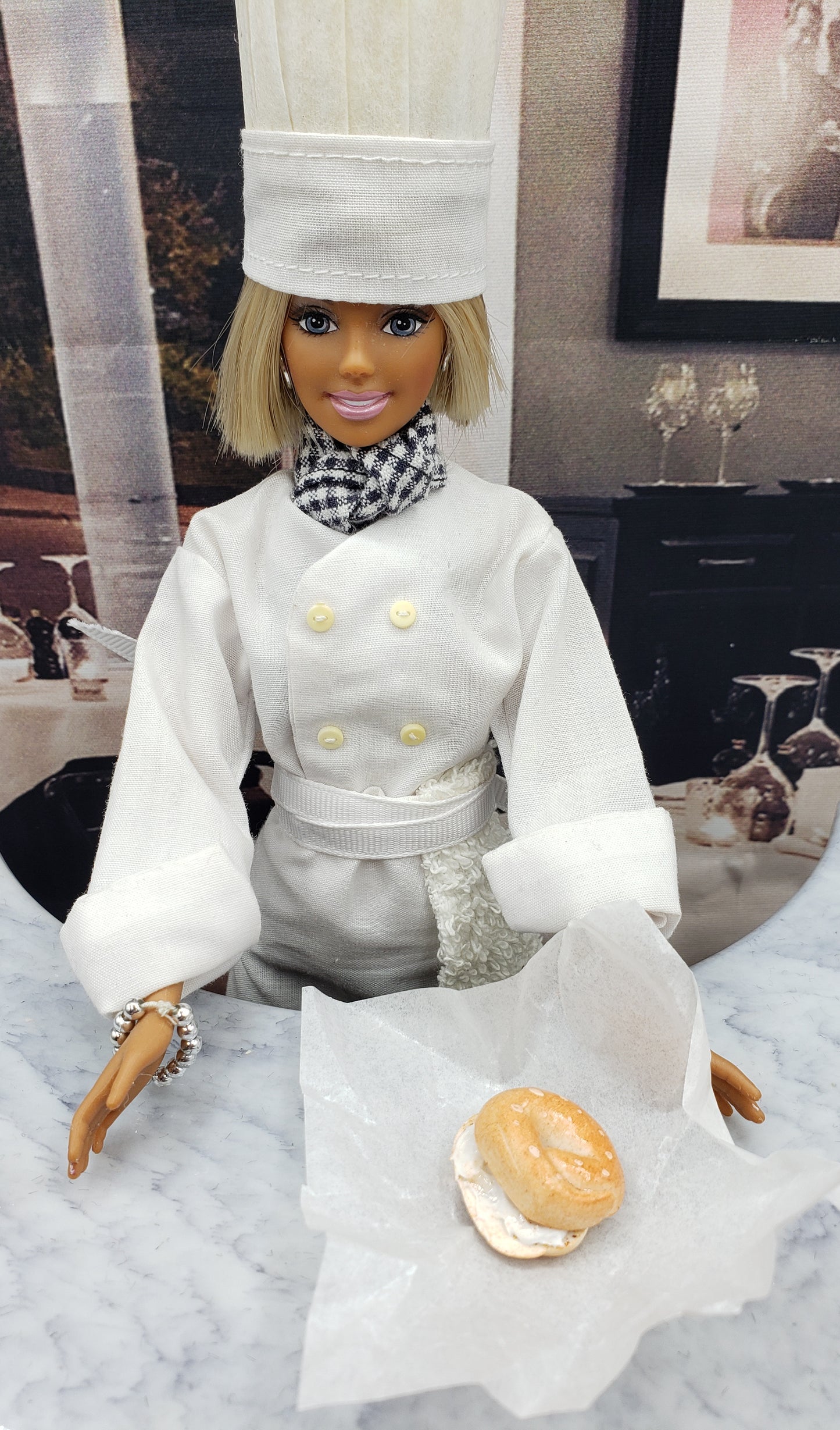 Chef Gina's miniature bagel with cream cheese held by a doll dressed as a chef on marble surface