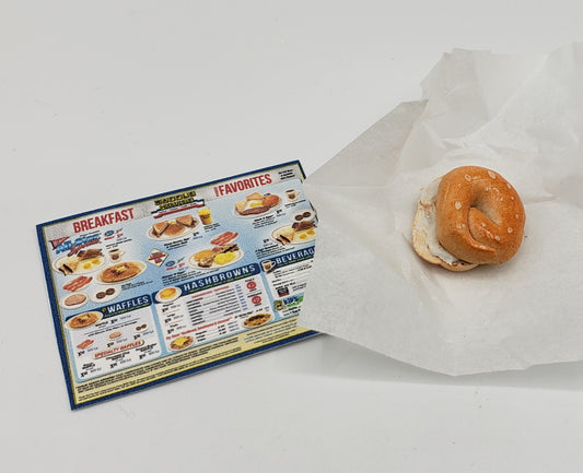 Miniature bagel with cream cheese from Chef Gina's Mini Food placed on white paper next to a breakfast menu