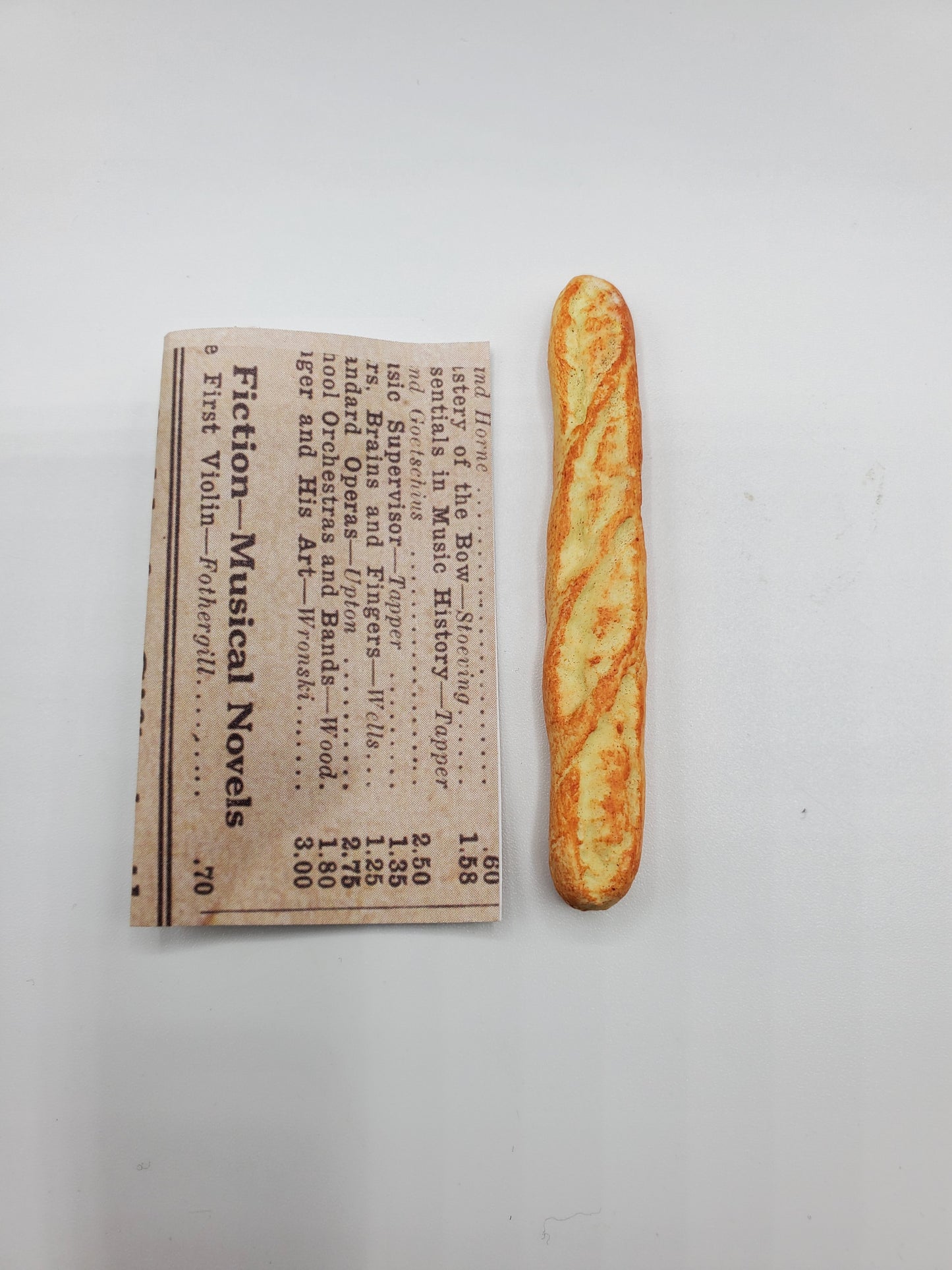 Chef Gina's Mini Food miniature baguette bread placed next to a folded newspaper on white background