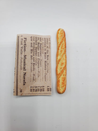 Chef Gina's Mini Food miniature baguette bread placed next to a folded newspaper on white background