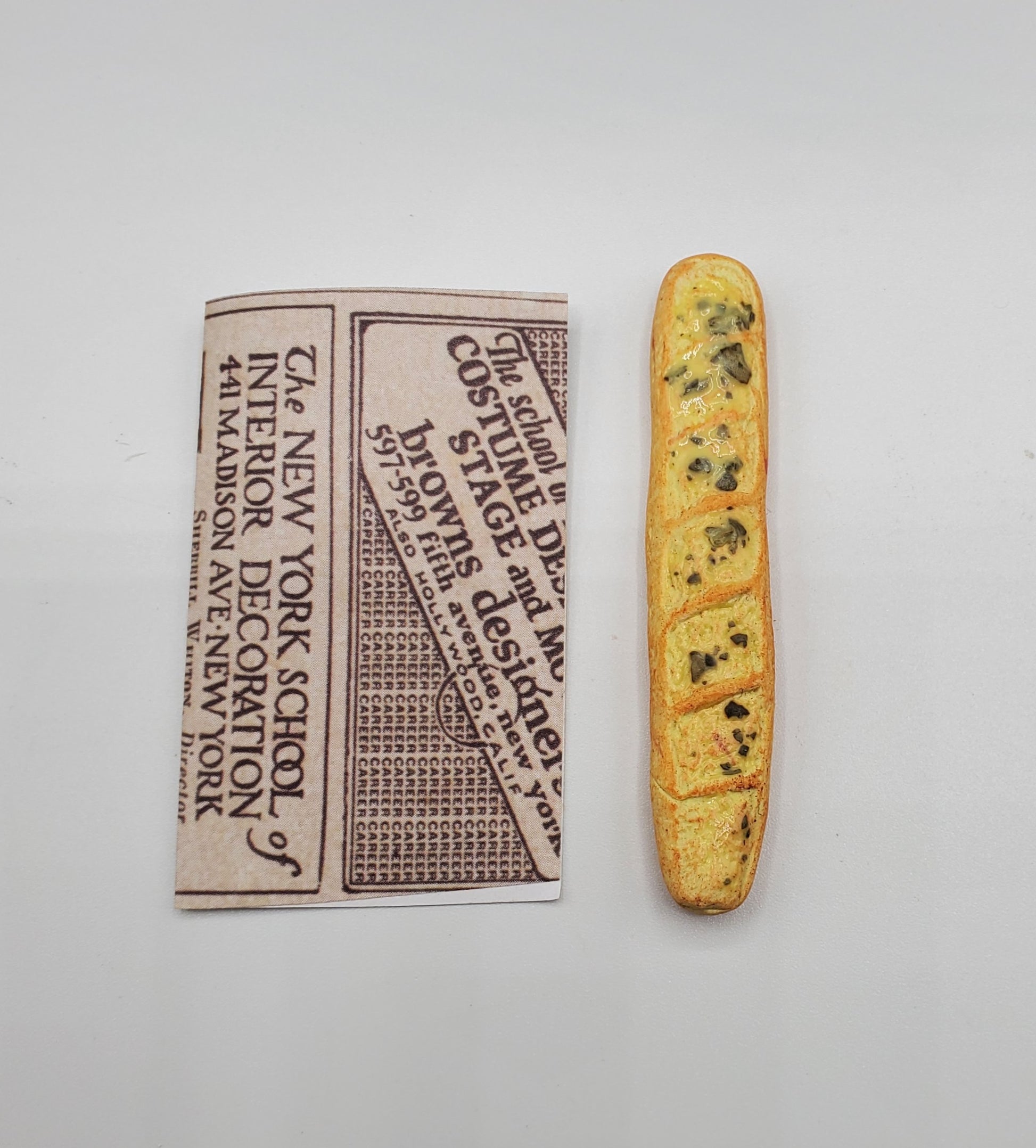Chef Gina's miniature baguette bread next to a folded piece of vintage newspaper on a white background