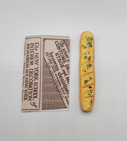 Chef Gina's miniature baguette bread next to a folded piece of vintage newspaper on a white background