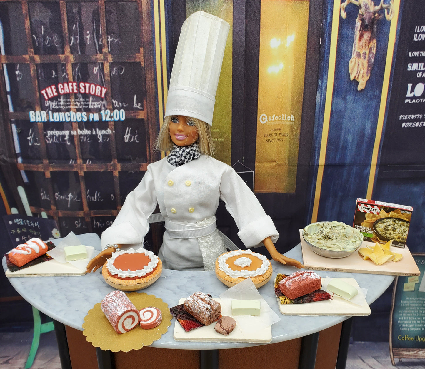 Miniature banana loaf for dolls displayed with other doll-sized desserts on a table with a doll chef in white uniform