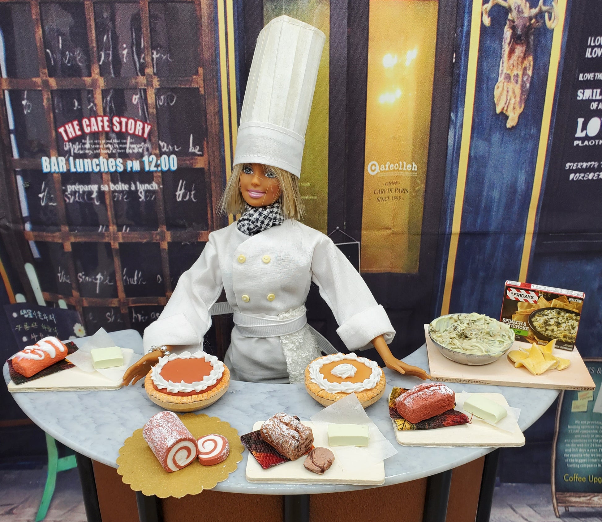 Chef doll in white uniform with miniature chocolate loaf bread and various pastries on a tabletop display