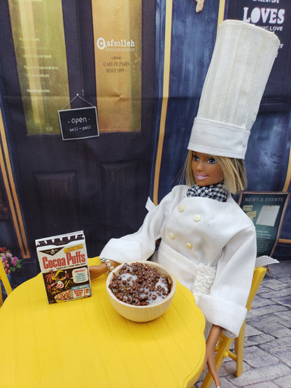 Chef Gina's miniature Coco Puffs cereal for dolls with doll chef in white outfit sitting at yellow table