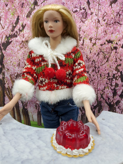 Miniature cranberry jello dessert displayed on a table in front of a doll wearing a festive sweater