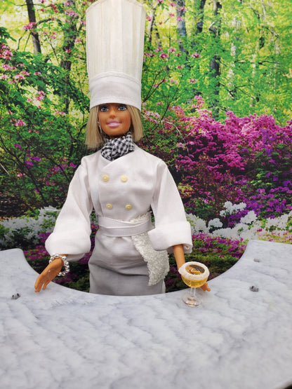 Chef Gina's doll dressed as a chef holding miniature margarita toy drinks in a garden setting