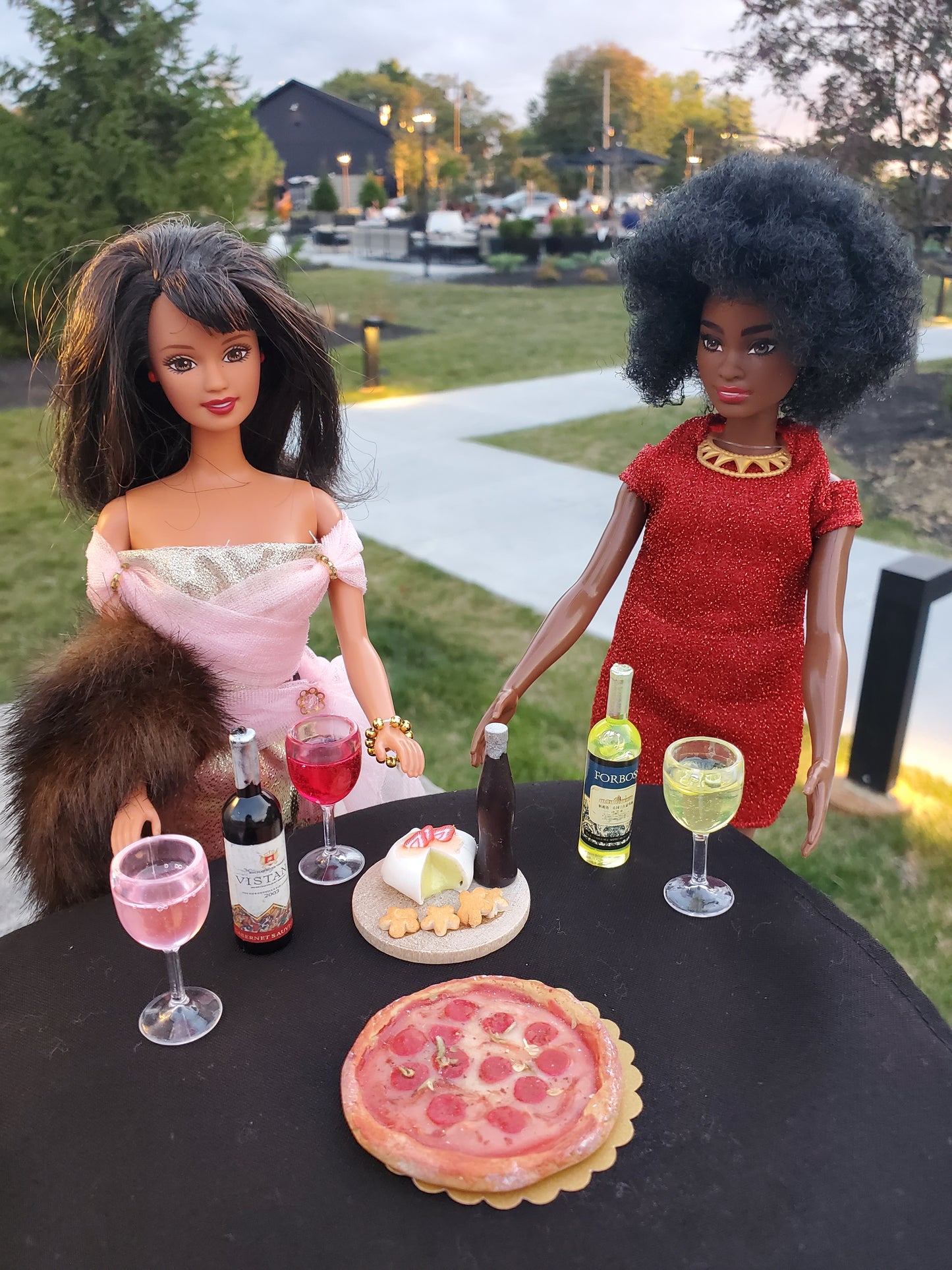 Miniature pink wine glass for dolls next to doll accessories including pizza and cheese platter