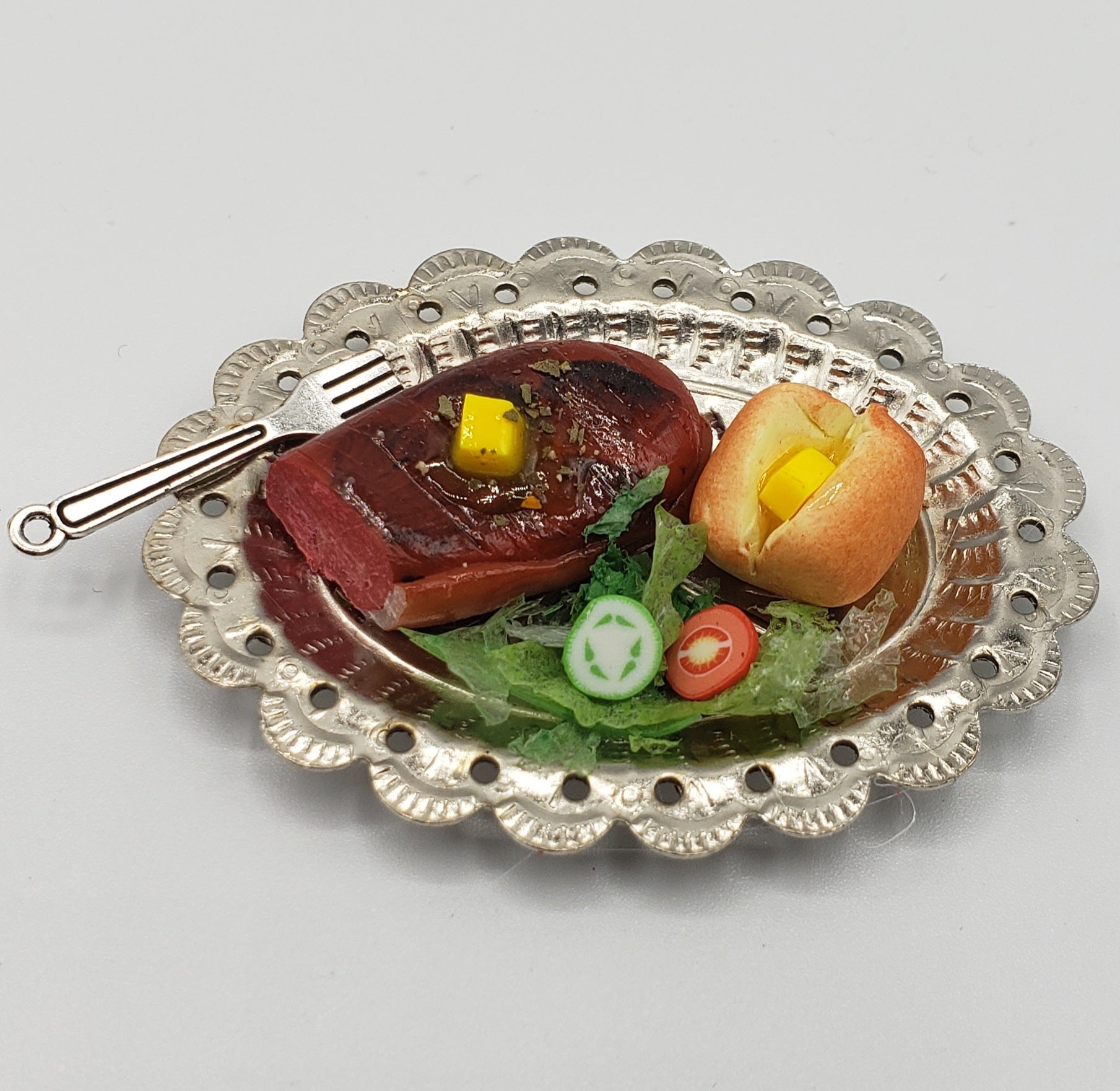 Chef Gina's miniature steak dinner set with steak, roll, greens, and fork on decorative silver plate