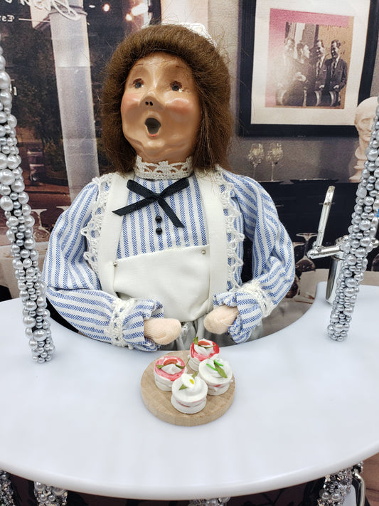 Miniature tea sandwiches served on a wooden plate with a decorative doll dressed in blue and white behind