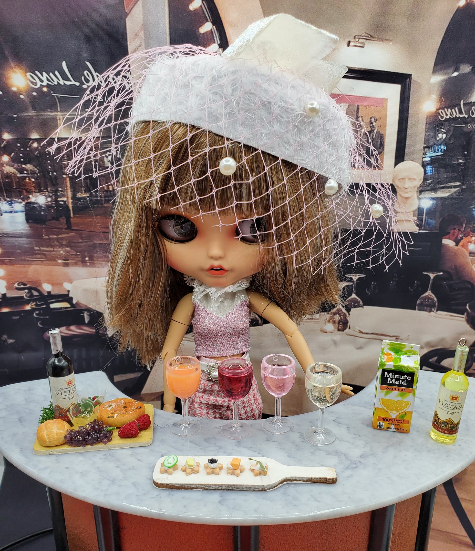 Doll with miniature white wine for dolls and various drink glasses displayed on a table
