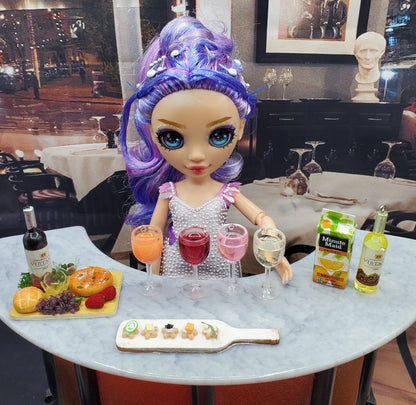 Doll with purple hair seated at table with miniature white wine for dolls and other miniature drinks and snacks