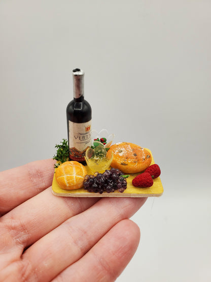 Miniature wine cheese tray with bottle of wine, grapes, bread, and raspberries held on fingertip