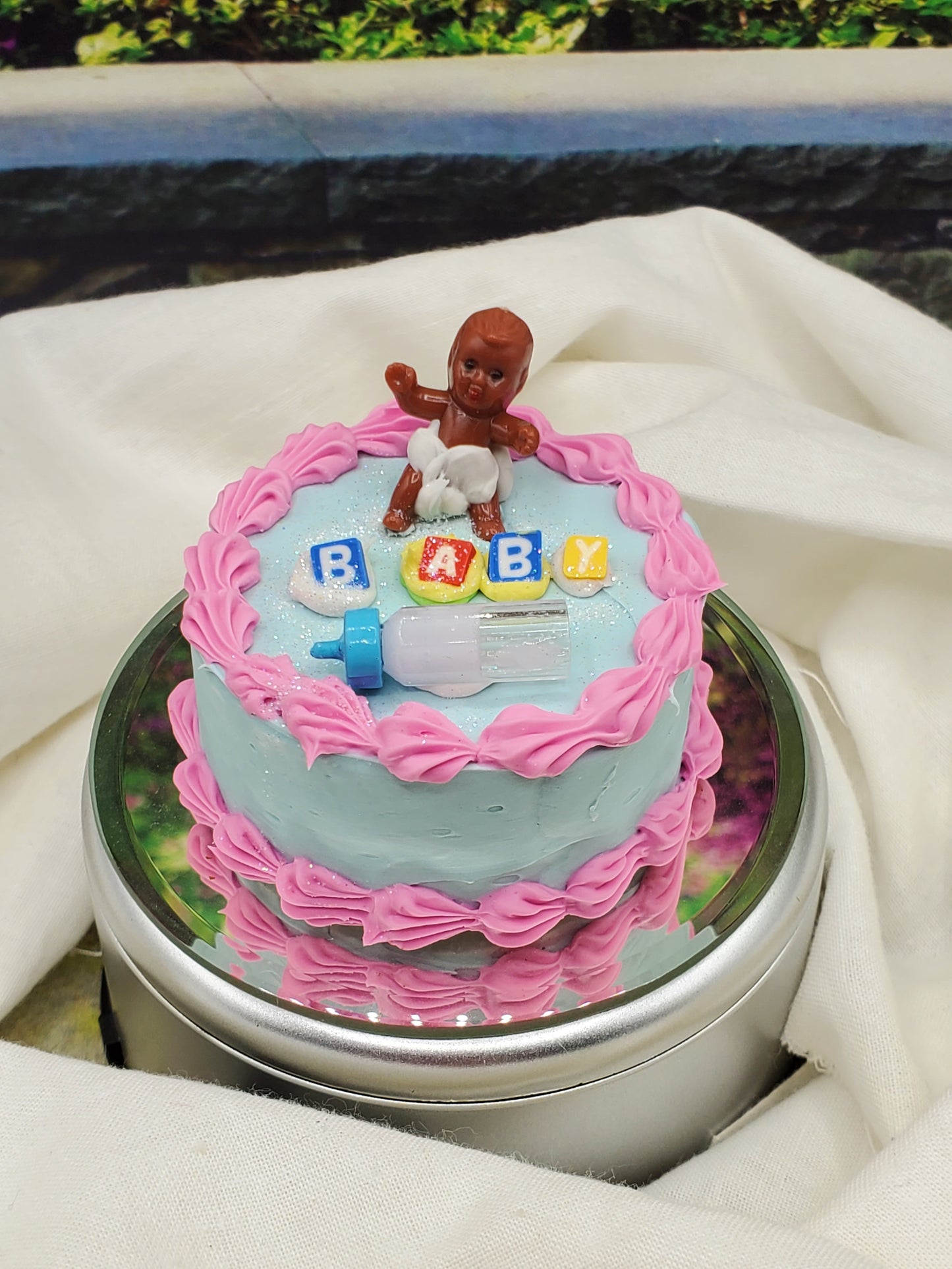 One sixth scale baby cake with pink icing, baby figurine, blocks spelling BABY, and a blue baby bottle