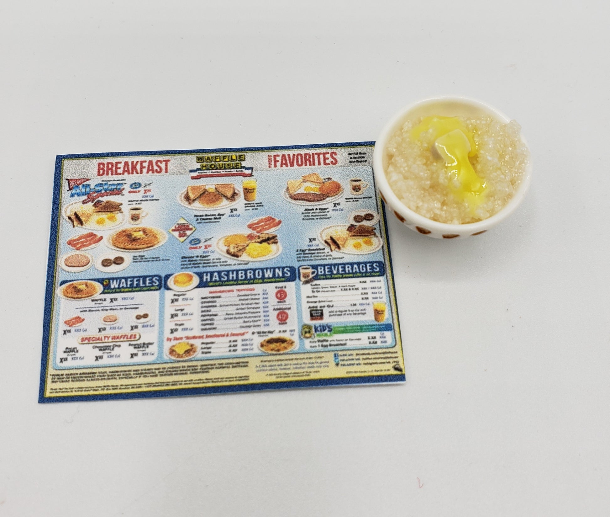 Chef Gina's one sixth scale grits miniature in a white cup with yellow butter on top next to a small breakfast menu