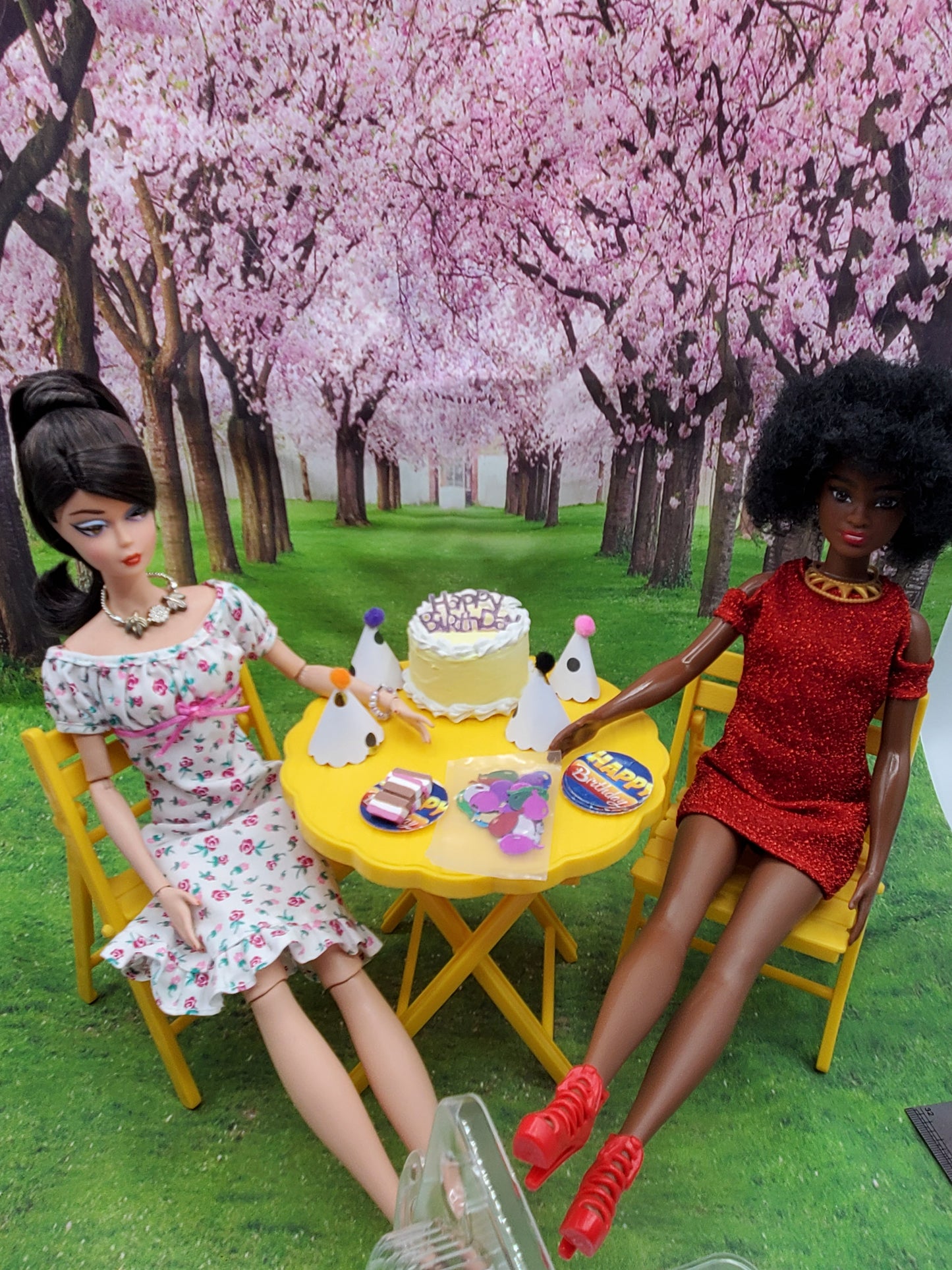 Chef Gina's pink flamingo doll party set featuring two dolls with dessert and party accessories at a yellow table under cherry blossom trees