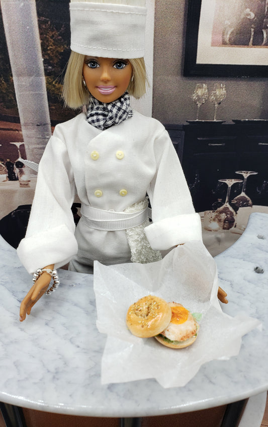 Chef Gina's realistic fried egg bagel sandwich for fashion dolls displayed on marble table with doll chef