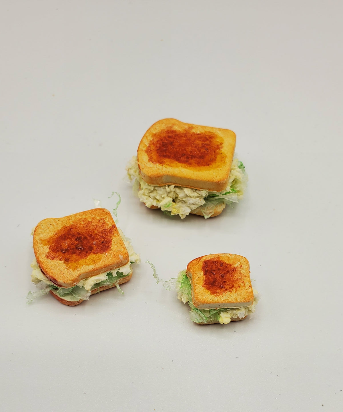 Three mini toasted sandwich halves with lettuce and creamy filling, arranged on a plain light background.