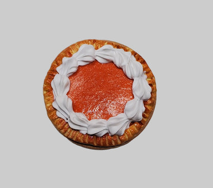 A miniature decorative pie figurine with orange-red filling, a brown crust, and white piped frosting, photographed from above on a plain light background.