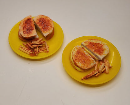 Two miniature yellow plates, each holding a small sandwich cut in half with fries, on a plain off-white surface.