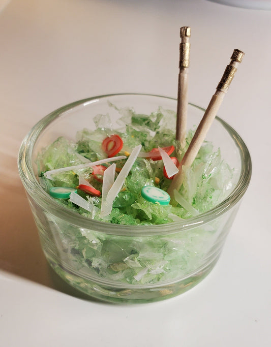 Clear glass bowl with green contents and skewers on a white background