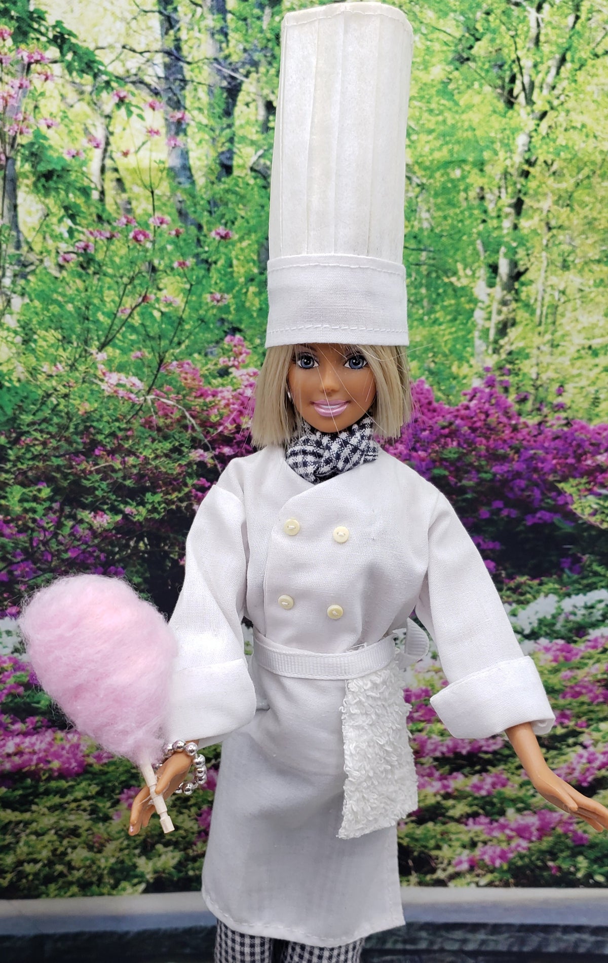Chef Gina's doll dressed as a chef holding 1:6 scale cotton candy for dolls in a garden background