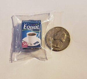 Miniature Equal sugar box next to a coin for size comparison in a clear package