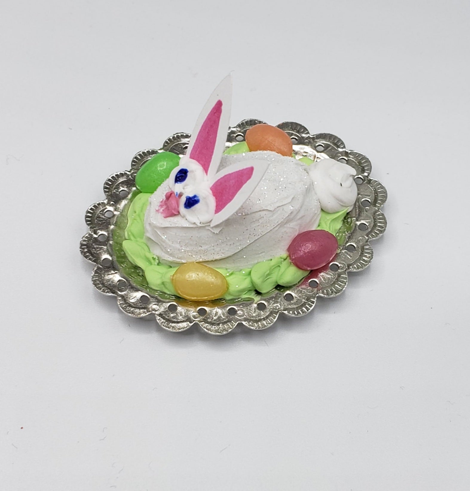 Fashion Doll size Easter bunny cake with white frosting and colorful candy eggs on a silver decorative plate